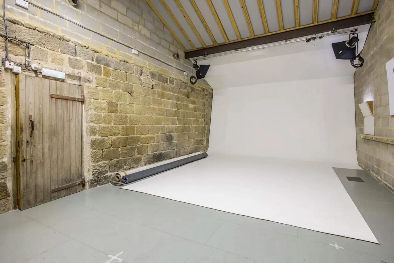 Empty studio space with stone brick walls, white flooring, striped awning ceiling and professional lighting rigs.