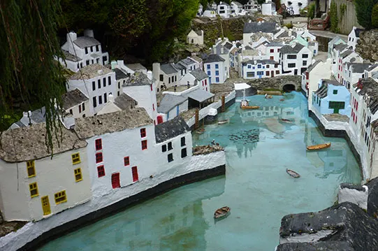 Miniature model village featuring white buildings with turquoise water canal and toy boats.