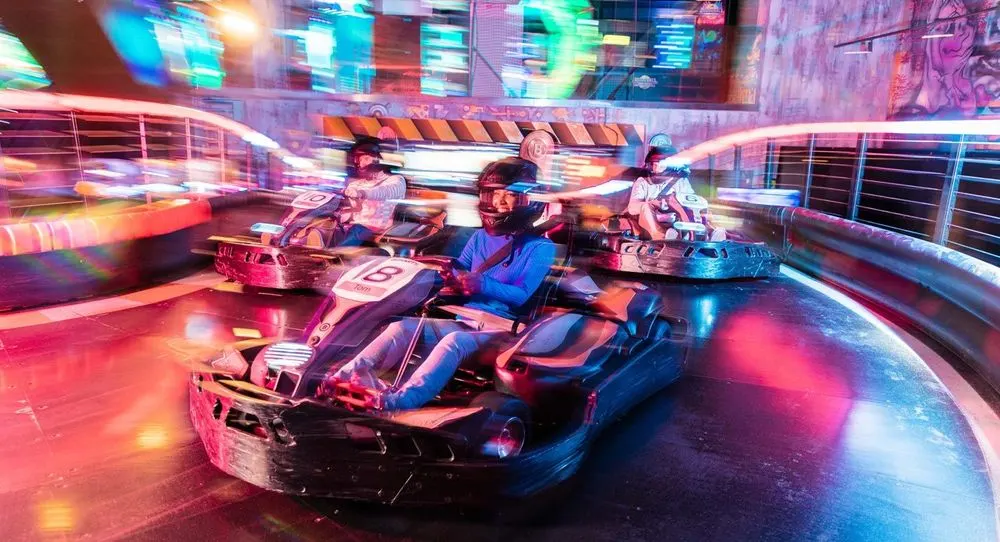 Multiple people driving bumper cars in a neon-lit indoor arena with motion blur.