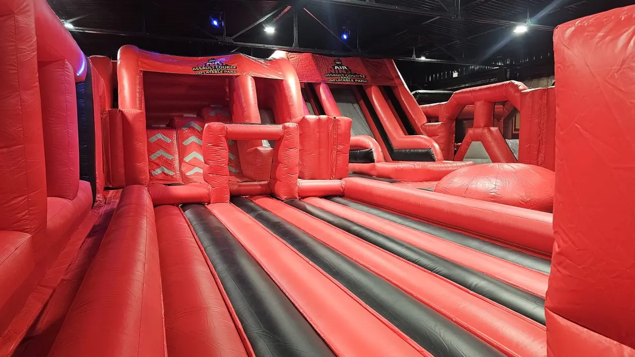 Red inflatable assault course with slides and obstacles inside an indoor leisure facility.