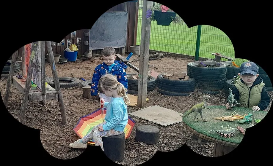 Young children playing in an outdoor adventure playground with tyres, wooden structures, and natural materials.