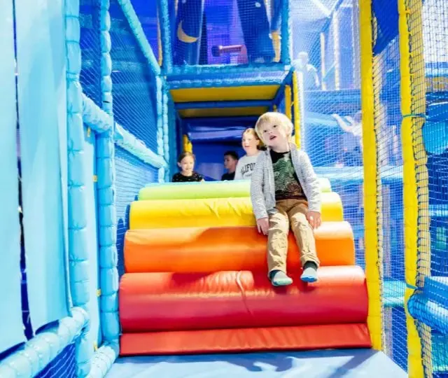 Young children playing on a colourful inflatable slide structure within an indoor play area.