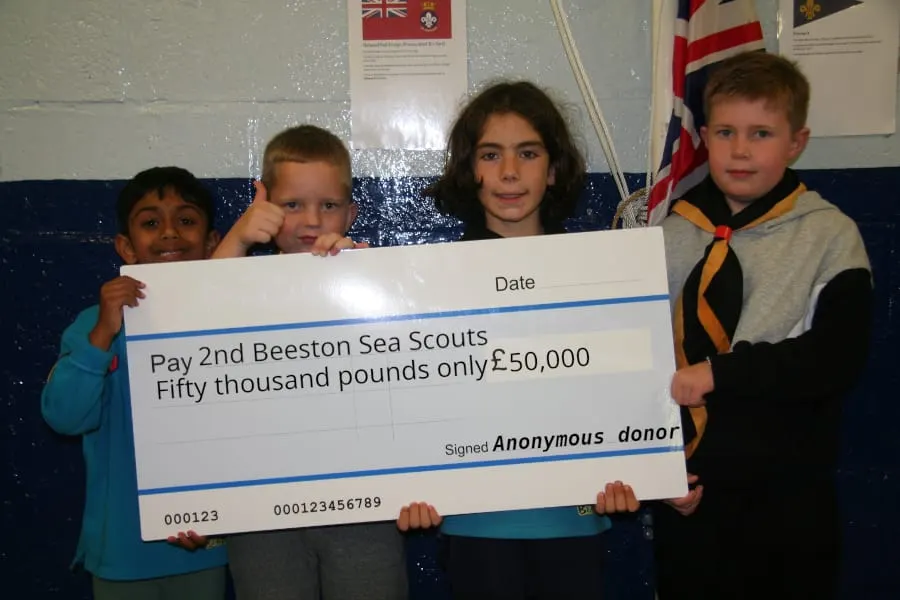 Four young Sea Scouts holding a large cheque for fifty thousand pounds from an anonymous donor.