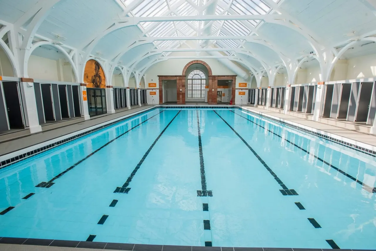 Empty indoor swimming pool with lane dividers under a grand arched white ceiling with skylights.