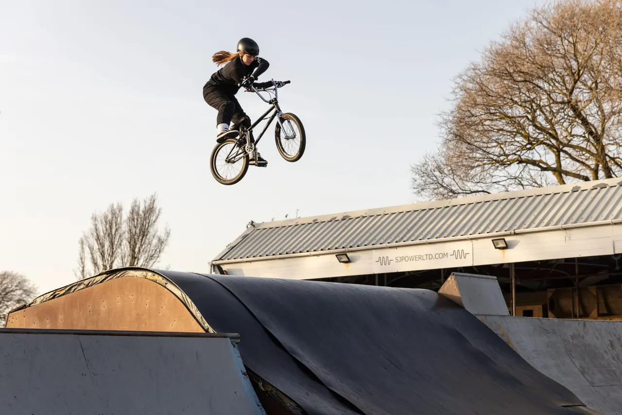 Person performing a jump on a bicycle over ramps at an outdoor skate park.