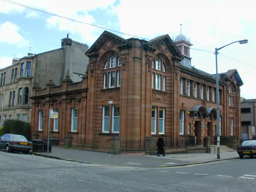 Victorian sandstone library building on a corner street with parked cars nearby.