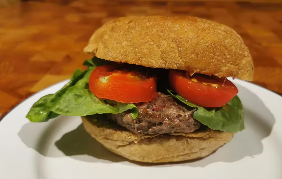 A burger with a wholemeal bun, beef patty, lettuce and tomato slices on a white plate.