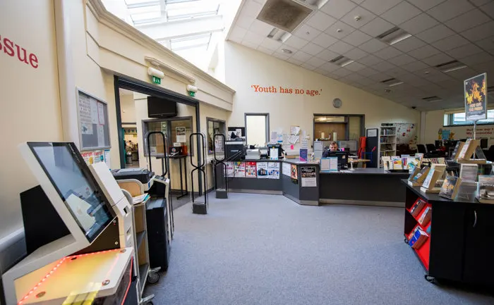 Interior of a modern library with interactive touchscreen display, reception desk, and shelving visible in the background.