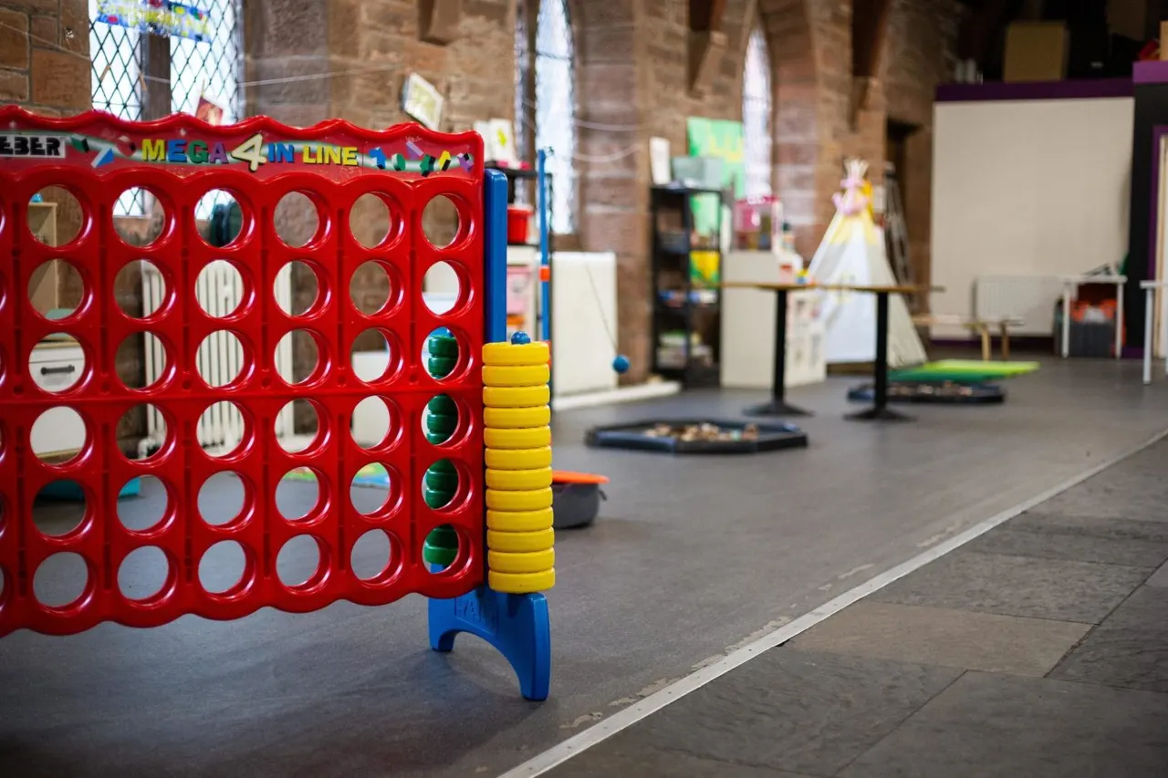 Giant Mega 4 in Line game and other play equipment in an indoor play space with brick walls.
