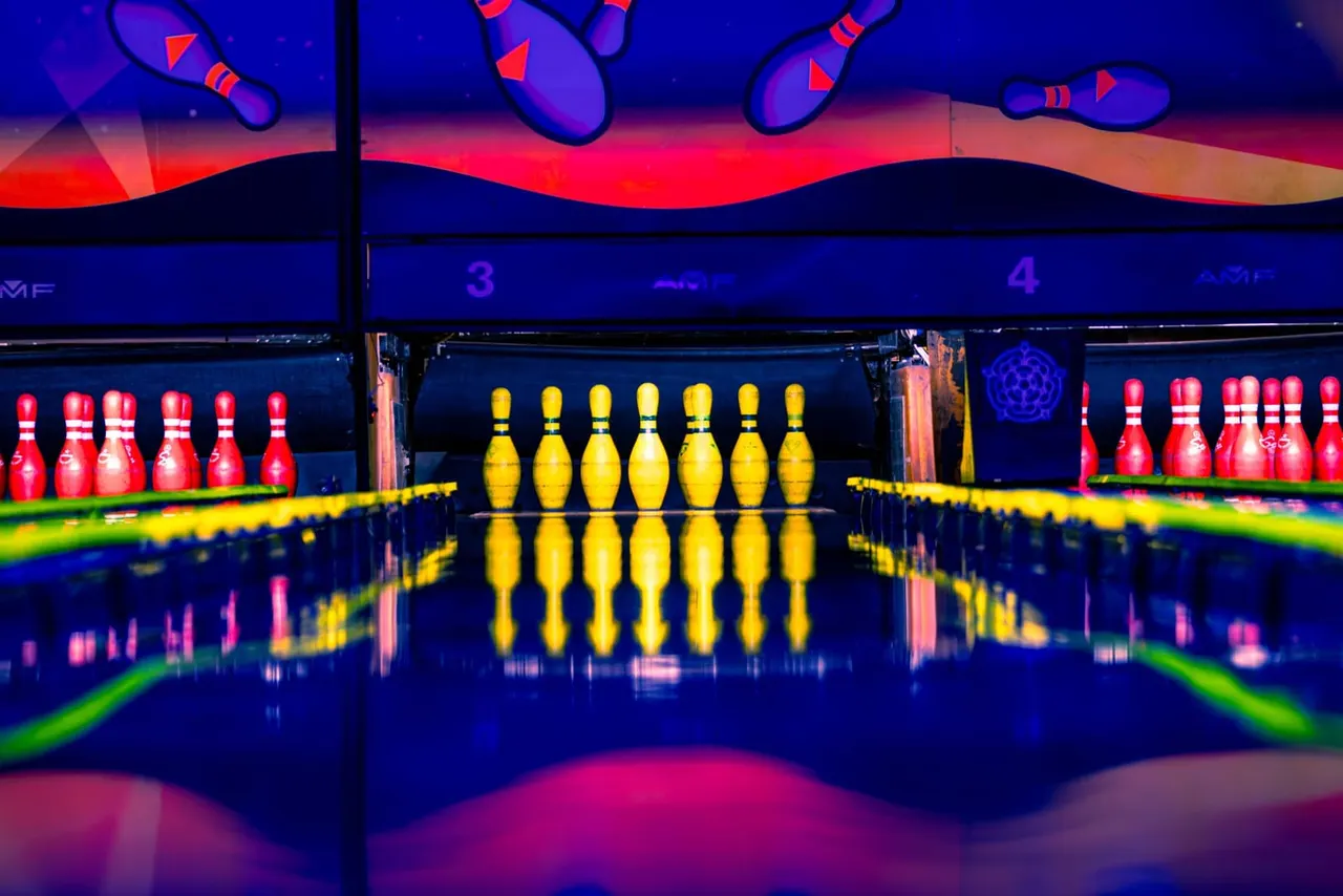 Neon-lit bowling alley with colourful pins set up on lanes, viewed from the bowler's perspective.