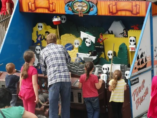 Children and adults playing at a Halloween-themed carnival game booth with skull and pumpkin decorations.