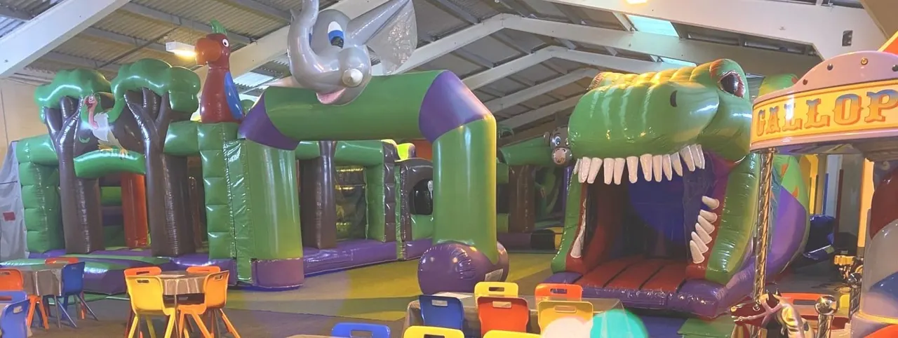 Indoor play area with colourful inflatable bouncy castles and themed structures in green, purple and red.