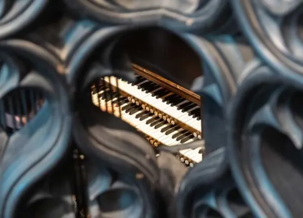 An illuminated organ keyboard viewed through ornate stone architectural detailing.
