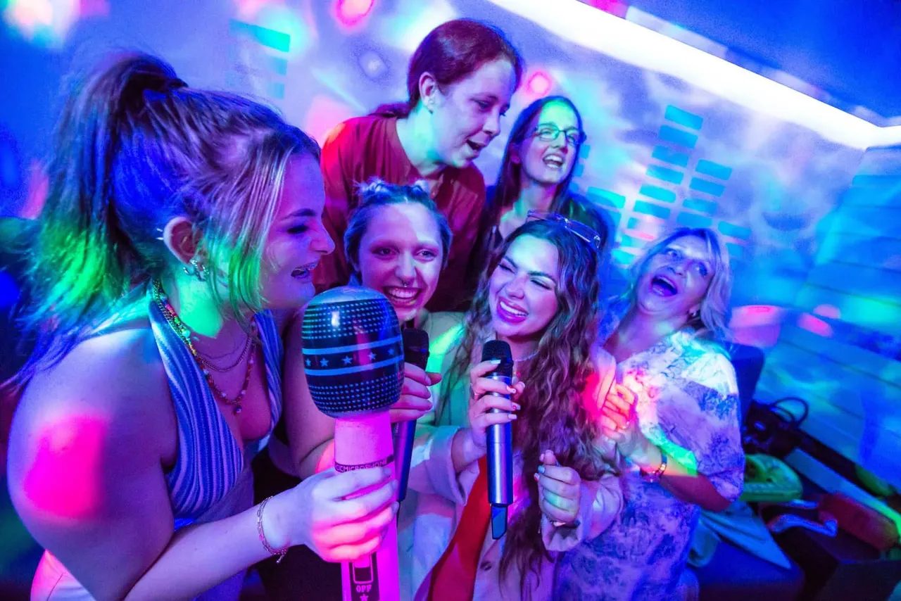 Group of young people singing karaoke together under colourful neon lighting in an entertainment venue.