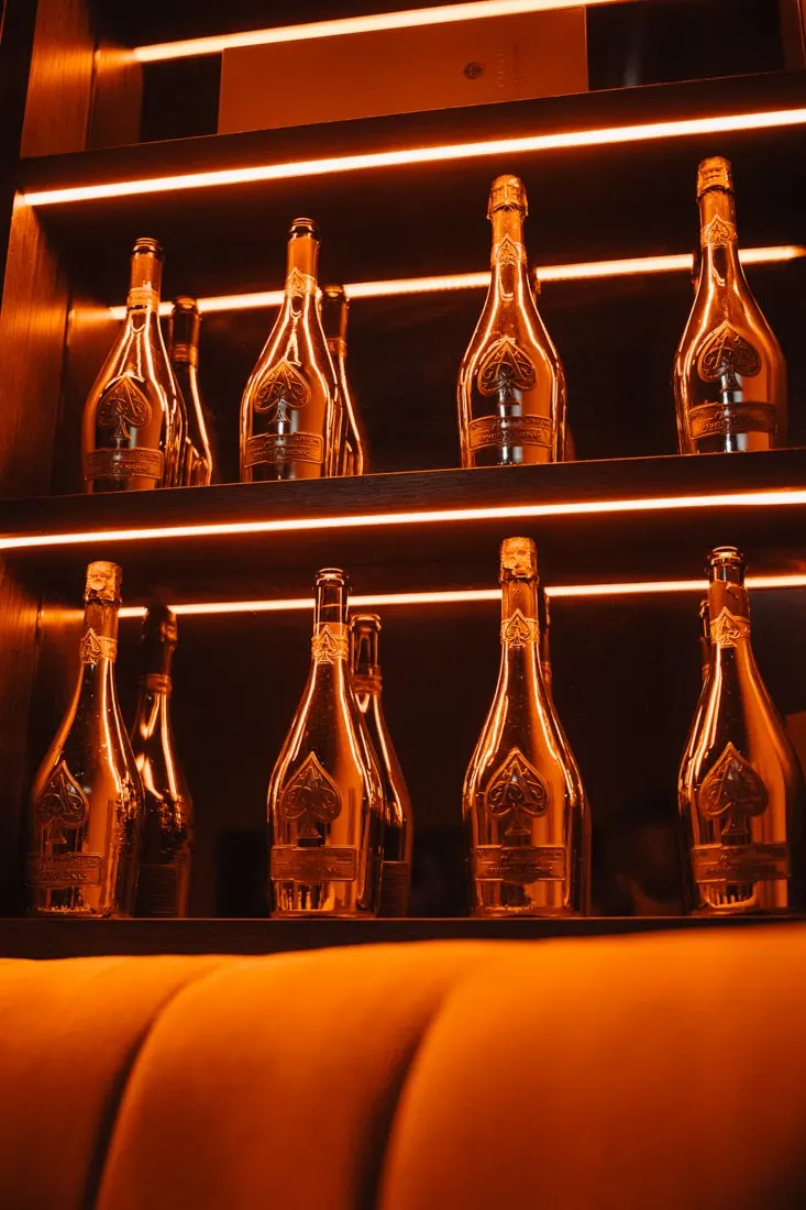 Champagne bottles displayed on illuminated shelves with warm orange neon lighting in a lounge bar setting.