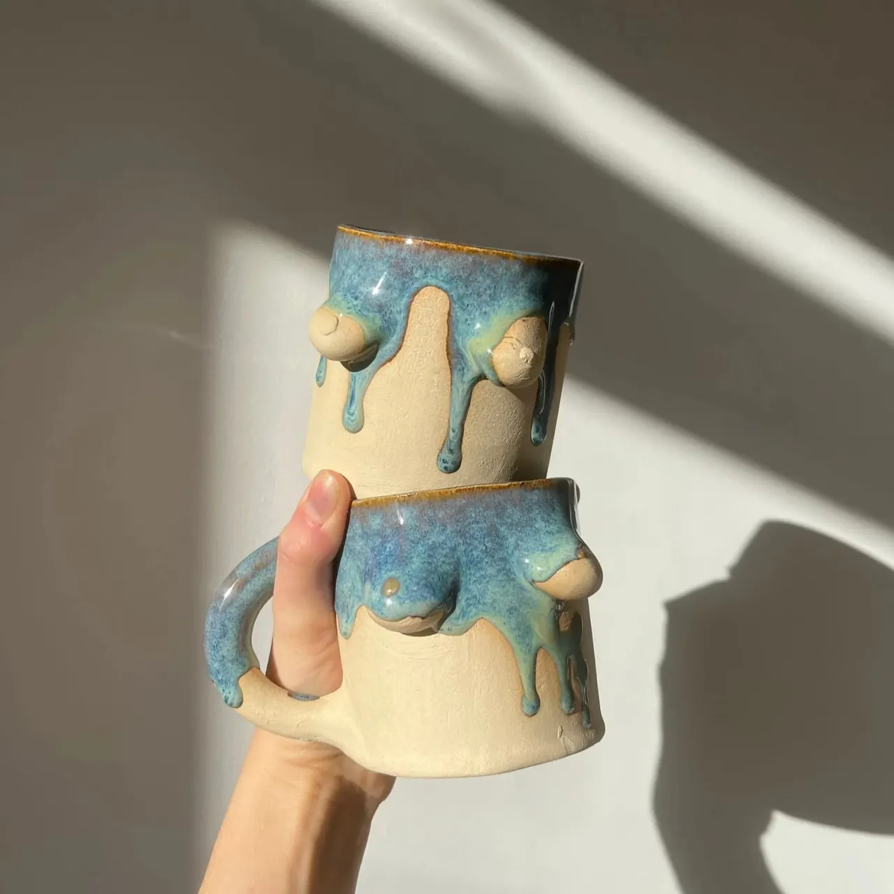 Hand holding a stacked ceramic vessel with cream and blue-glazed sections featuring decorative sculptural details.