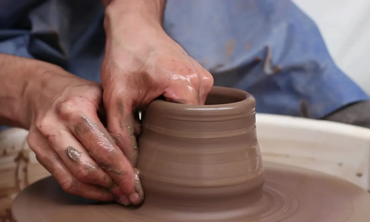 Hands shaping wet clay on a pottery wheel to form a vessel.