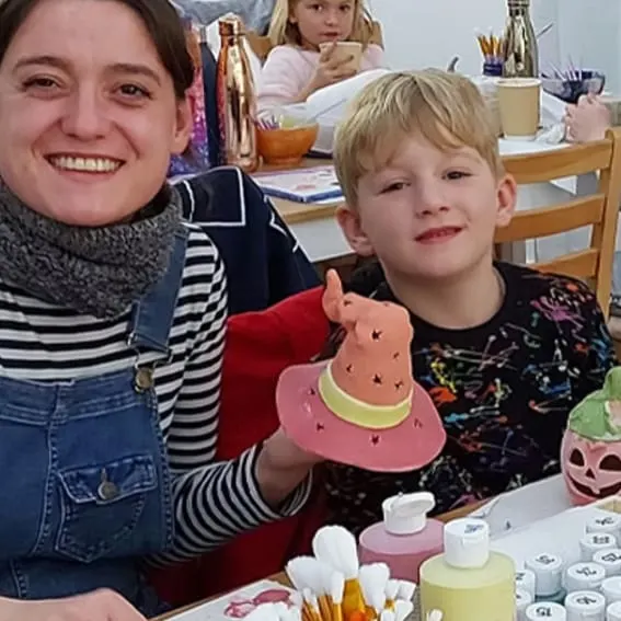 Young woman and boy at a craft table holding a painted ceramic llama figure.