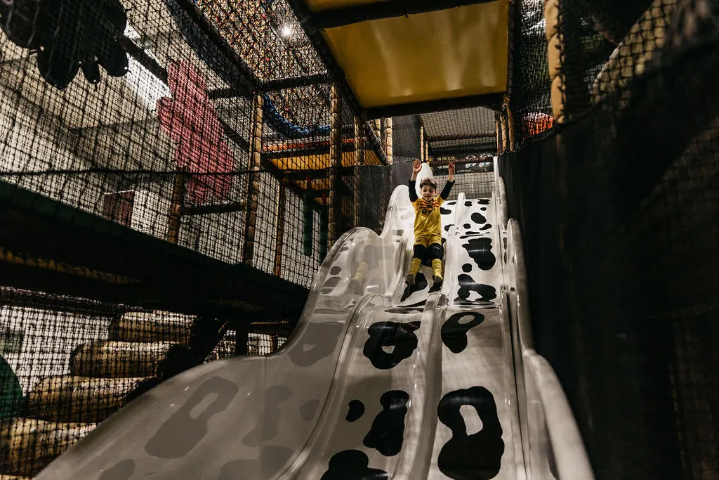 Child sliding down a white slide with cow-print design inside a netted play structure.