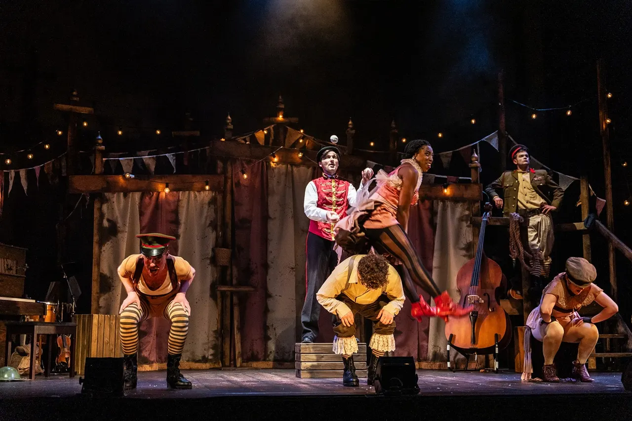 Circus performers in colourful costumes perform on a theatrical stage set with warm lighting and bunting.