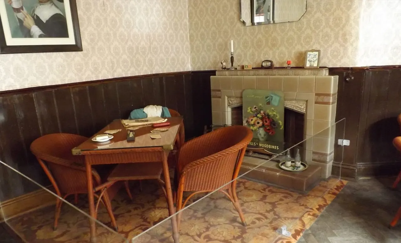 Retro-styled dining booth with two wooden chairs, small table set for service, fireplace, and period wallpaper in a pub interior.