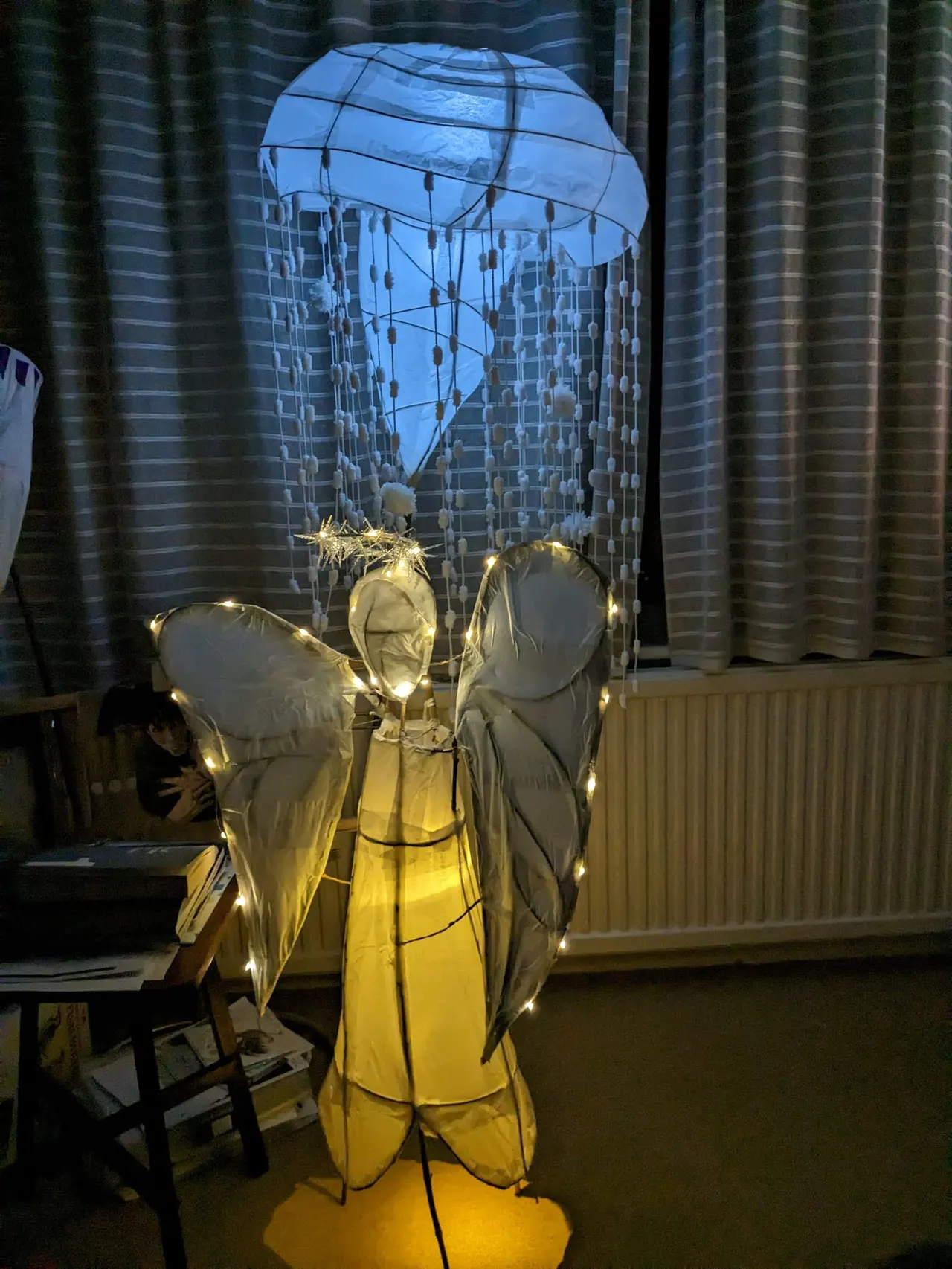 Illuminated jellyfish art installation with dangling tentacles, displayed indoors with curtained backdrop.