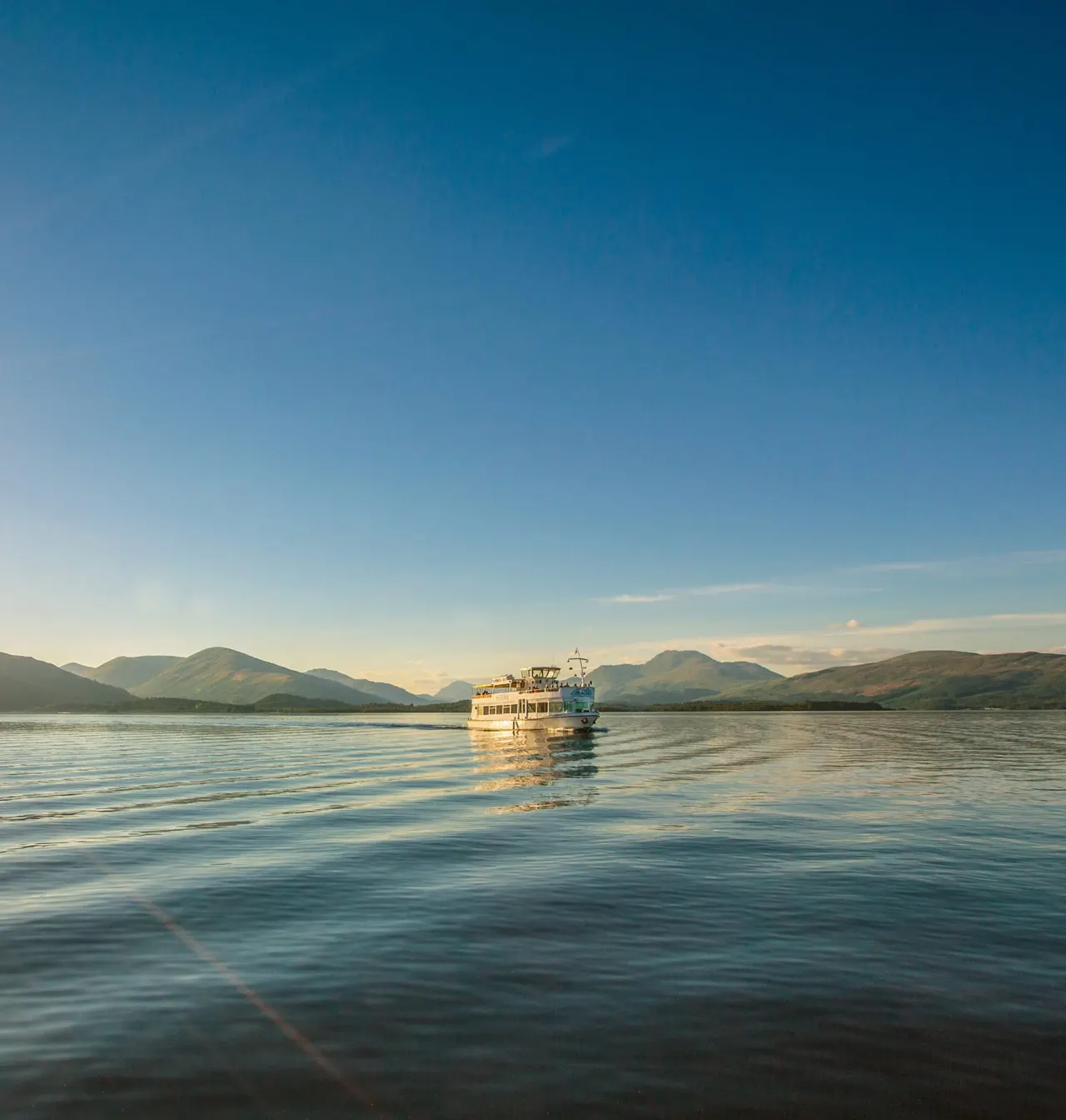 Passenger cruise boat on calm water with mountains in the background under clear blue sky.