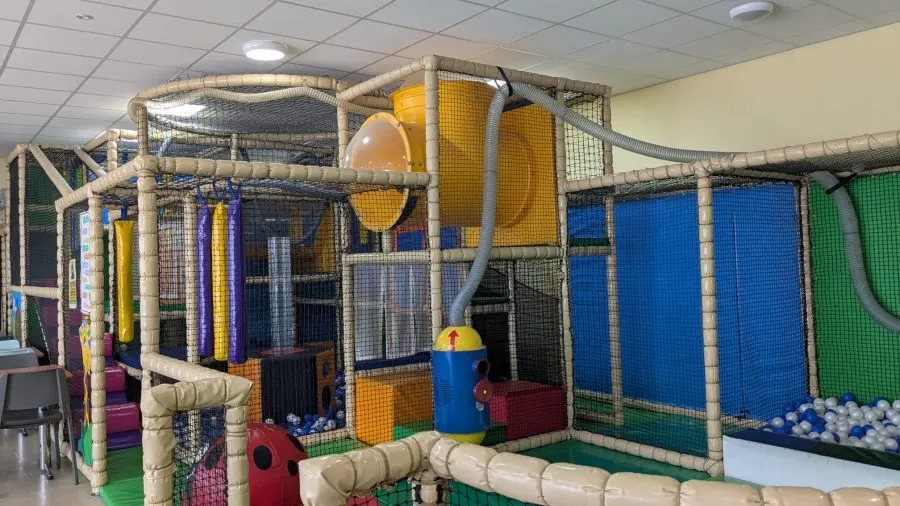 Indoor soft play structure with tunnels, slides, ball pit and climbing features in a leisure facility.