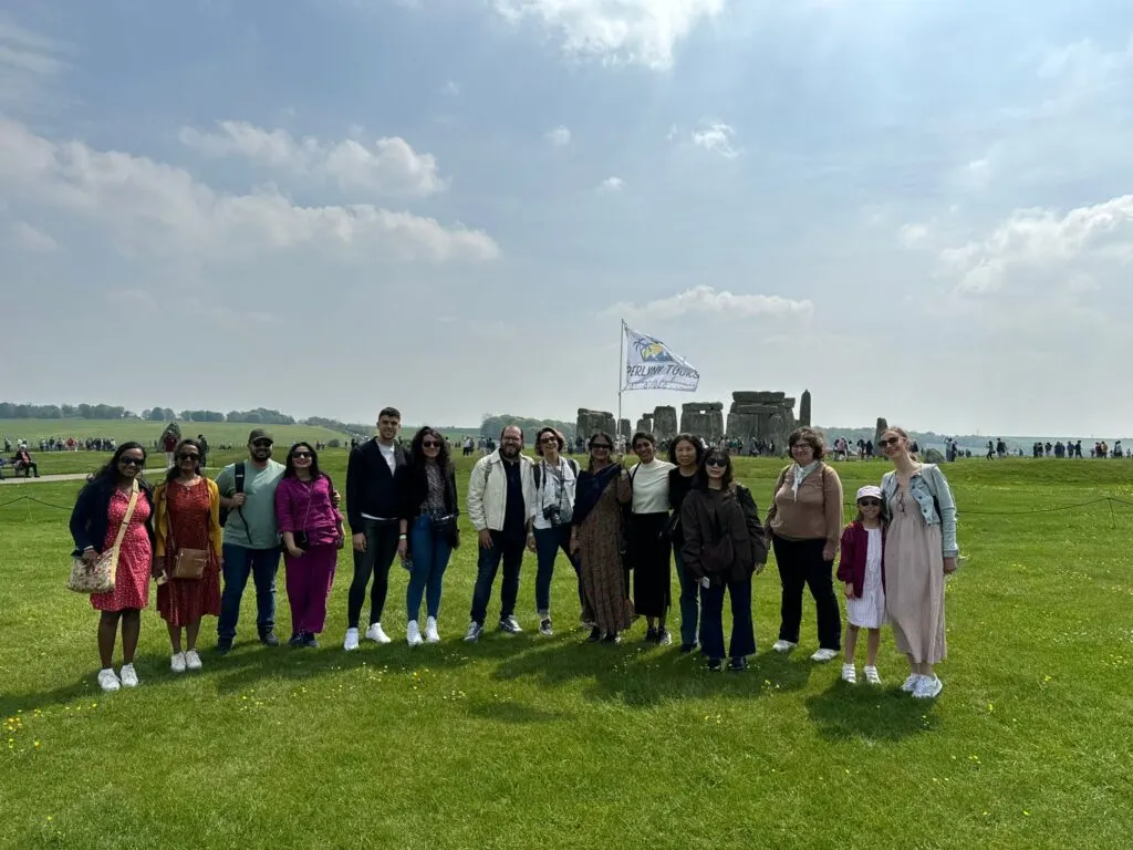 Group of visitors posing together on grassland with Stonehenge monument visible in the background.