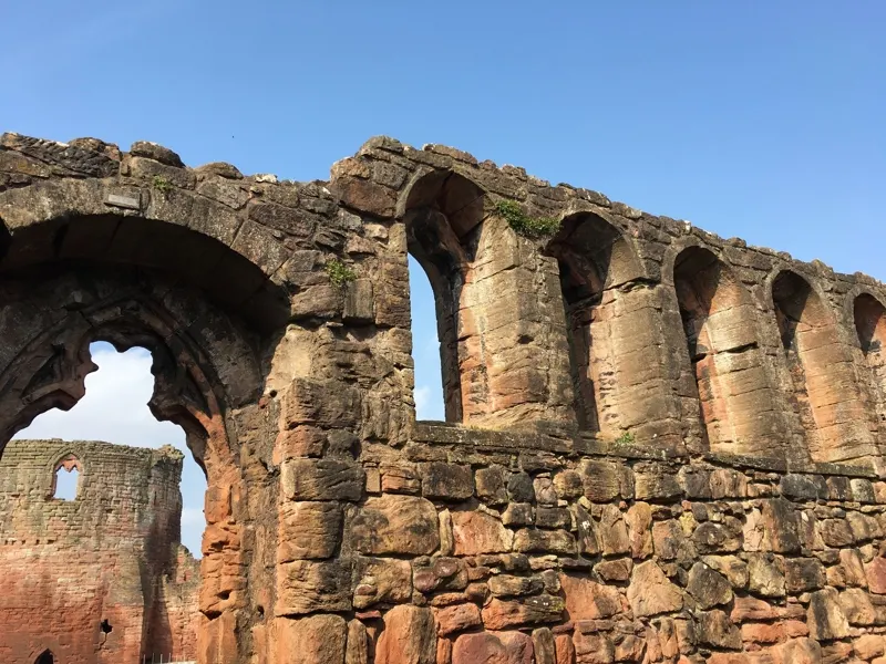 Ruined stone arches and walls of a medieval castle against a clear blue sky.