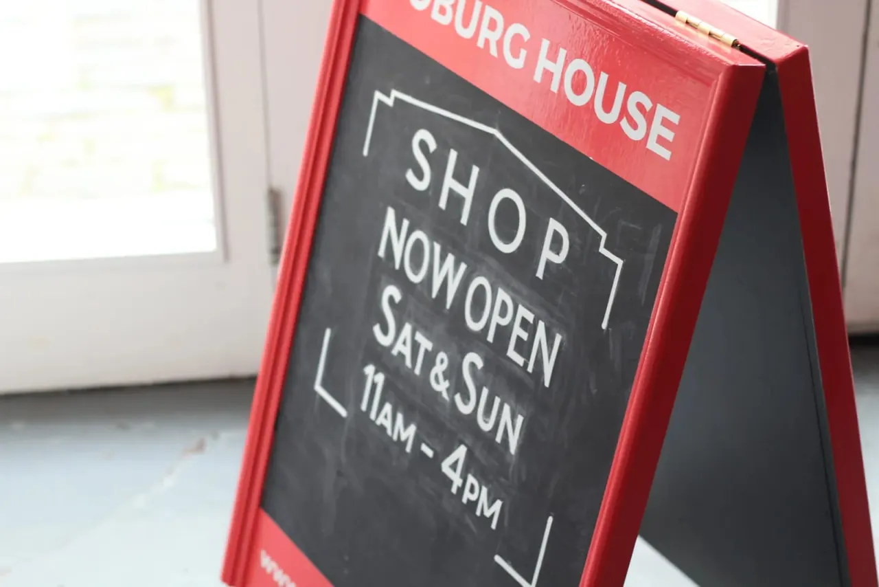 A-frame pavement sign with red frame advertising a burger house shop now open on Saturday and Sunday from 11am to 4pm.