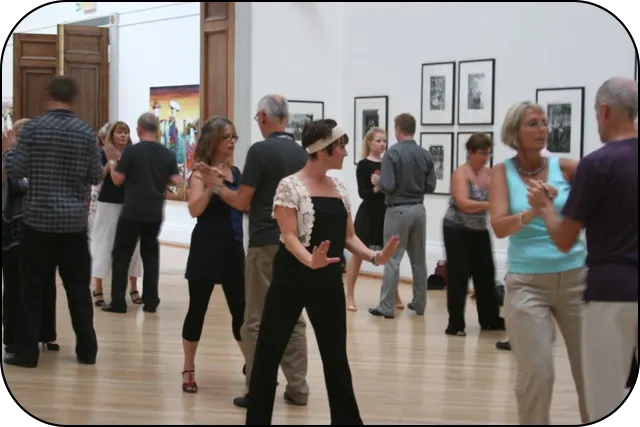 Adults dancing together in a studio with framed artwork on the walls.