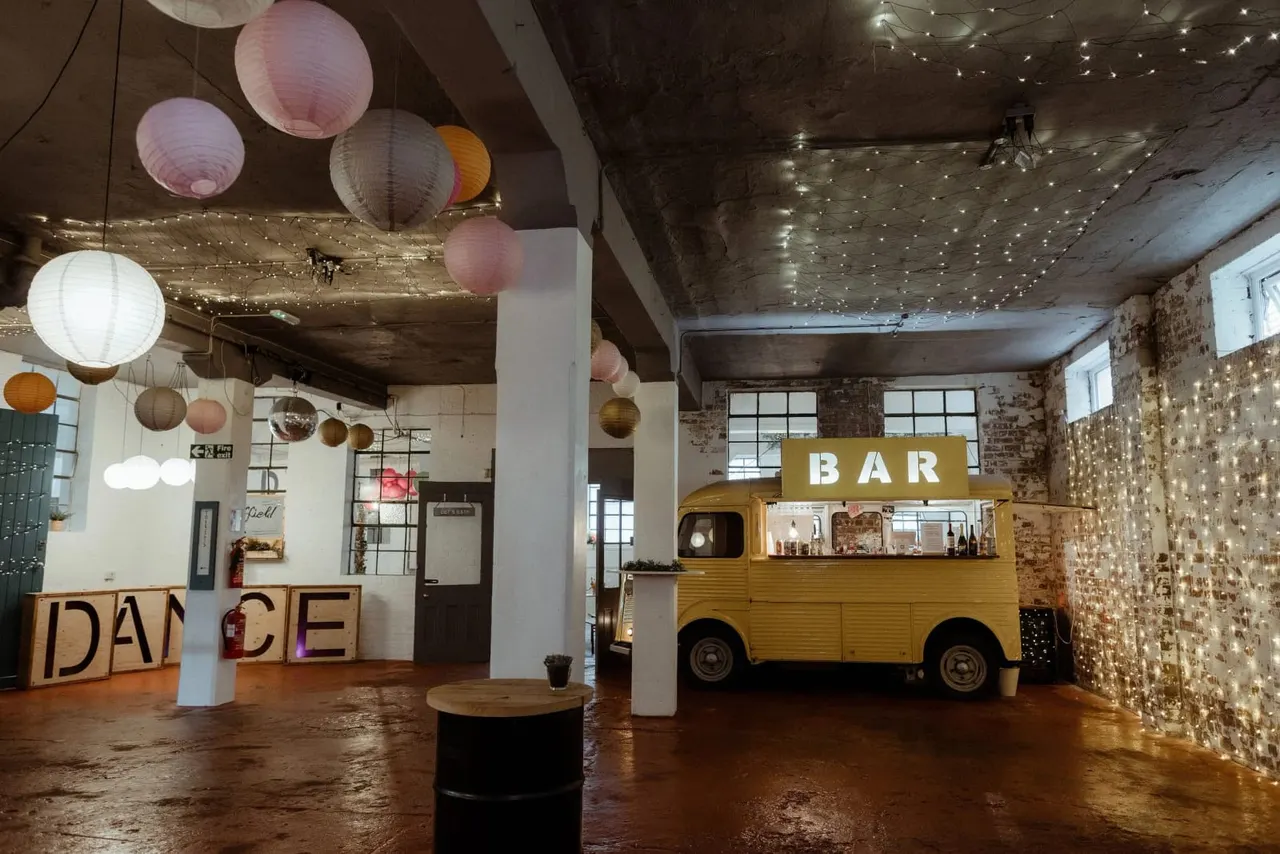 Industrial event space with yellow vintage van bar, dance floor, string lights and paper lantern decorations.