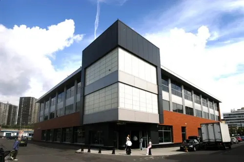 Modern brick and glass library building with angular architecture under blue sky with white clouds.