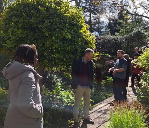 Group of visitors strolling through a garden path lined with hedges and trees.