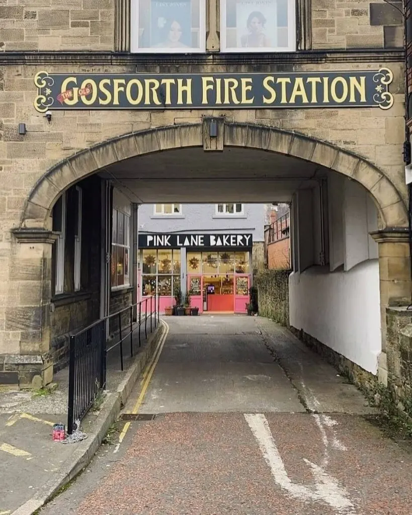 Arched stone passageway under Gosforth Fire Station leading to Pink Lane Bakery storefront with pink shopfront.