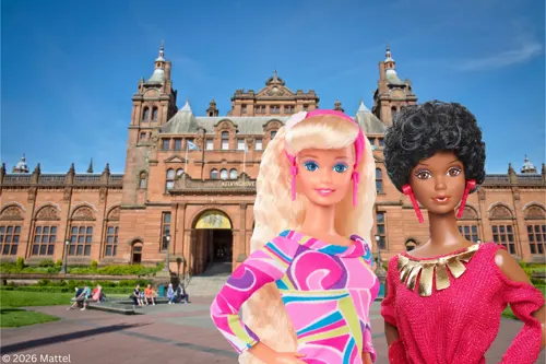 Two fashion dolls posed in front of Kelvingrove Art Gallery and Museum's red sandstone Victorian building.