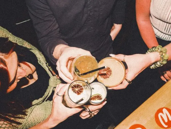 People holding artisanal cocktails with citrus garnishes and wooden accents at a bar.