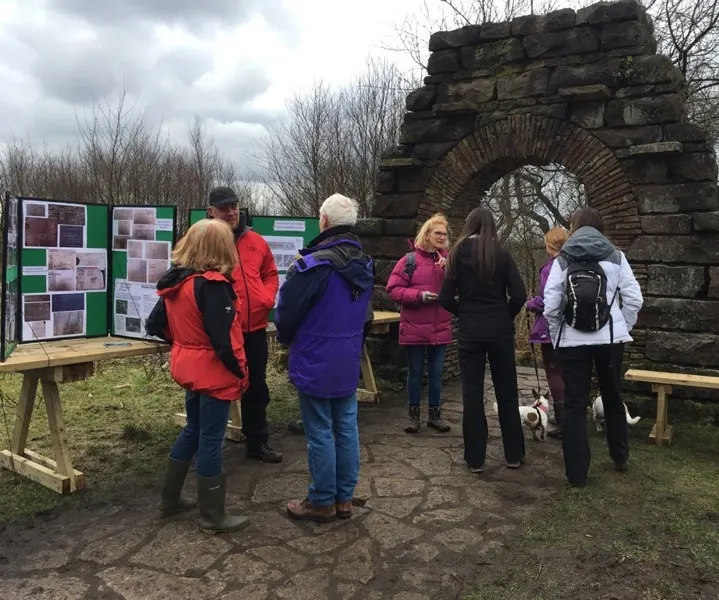 Visitors gathered outdoors at a historic stone arch, viewing information panels on wooden stands.