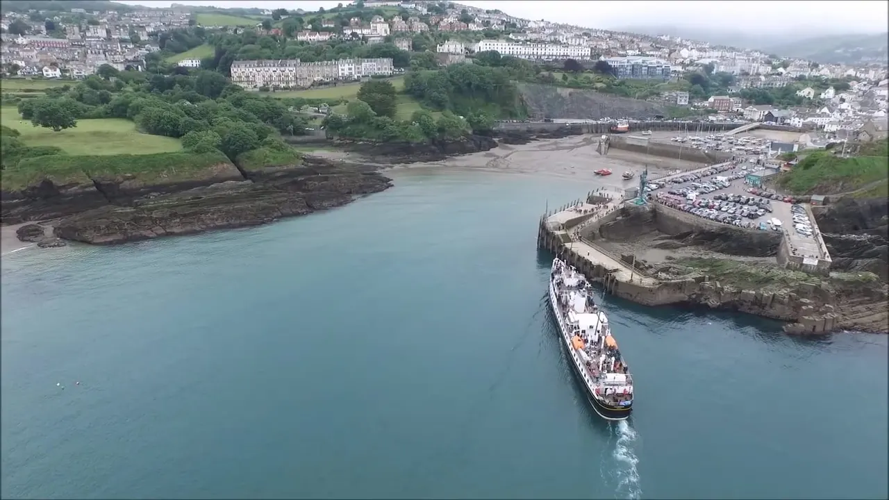 Cruise ship departing a coastal harbour surrounded by hillside buildings, harbours and sandy beaches.