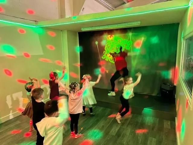Children dancing and playing in an interactive room with green and red light projections on walls and floor.