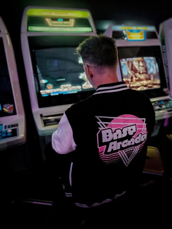 Person playing a vintage arcade machine in a dimly lit arcade hall with multiple cabinets.
