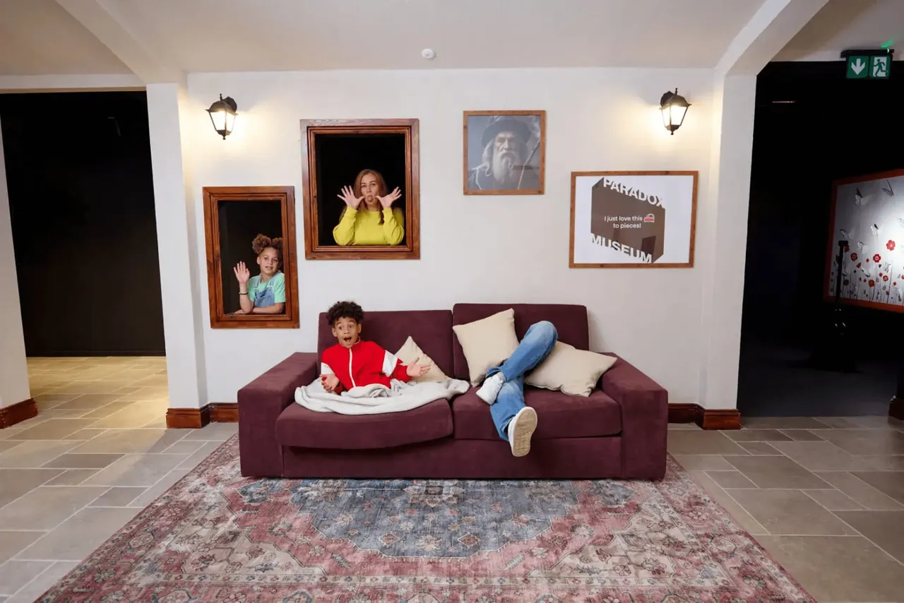Children pose playfully on a burgundy sofa and in framed wall portraits within an interactive museum gallery space.