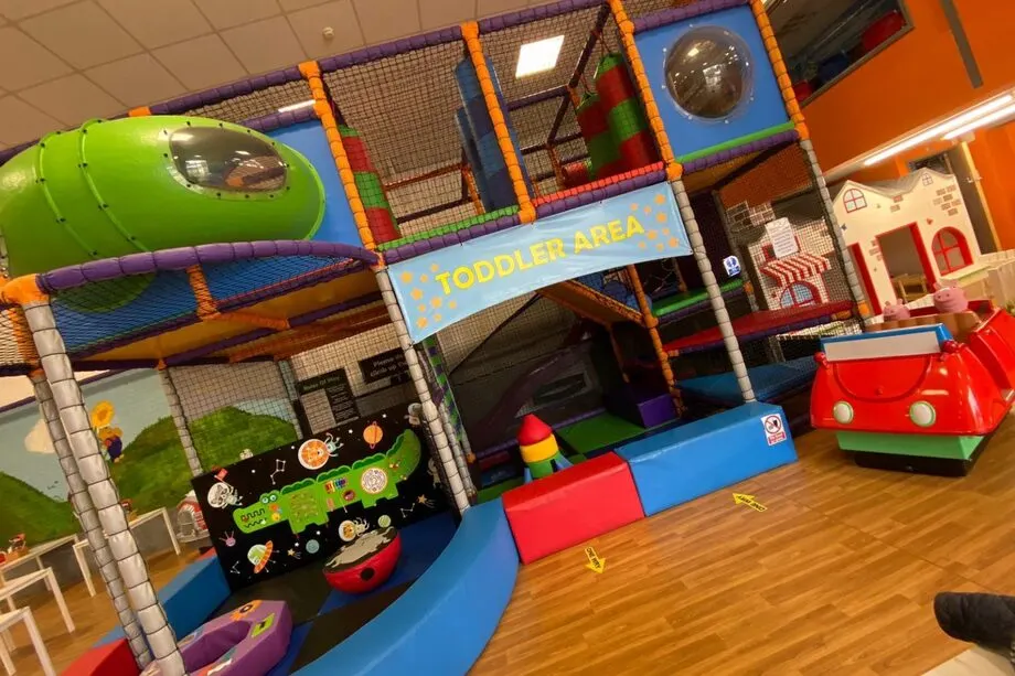 Colourful indoor play area with climbing structures, slides and soft play equipment for young children.