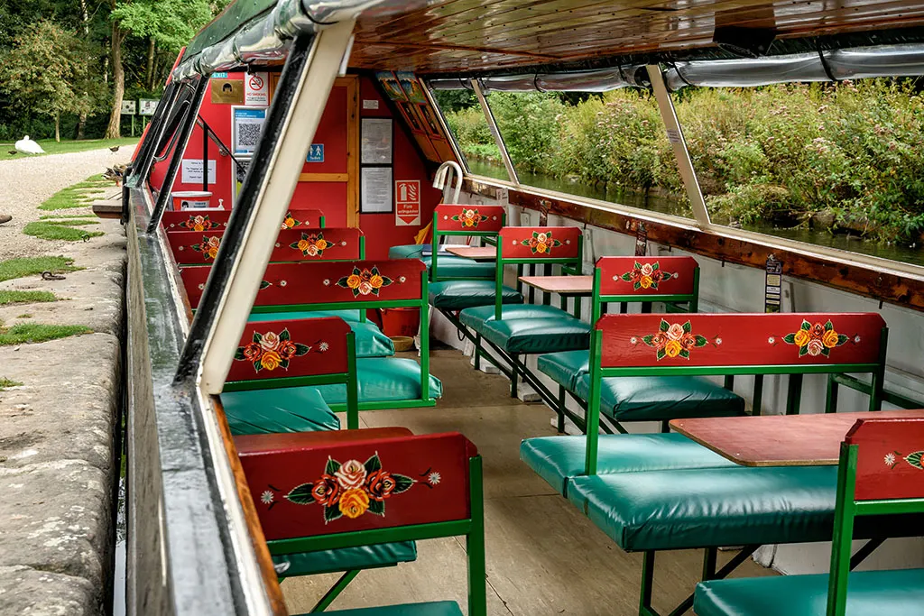 Interior of a narrowboat with green and red seating booths decorated with floral designs, set up for passenger tours.