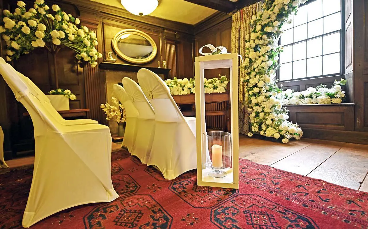 Elegantly decorated interior room with yellow chair covers, abundant yellow and white floral arrangements, and candlelit décor for a formal event.