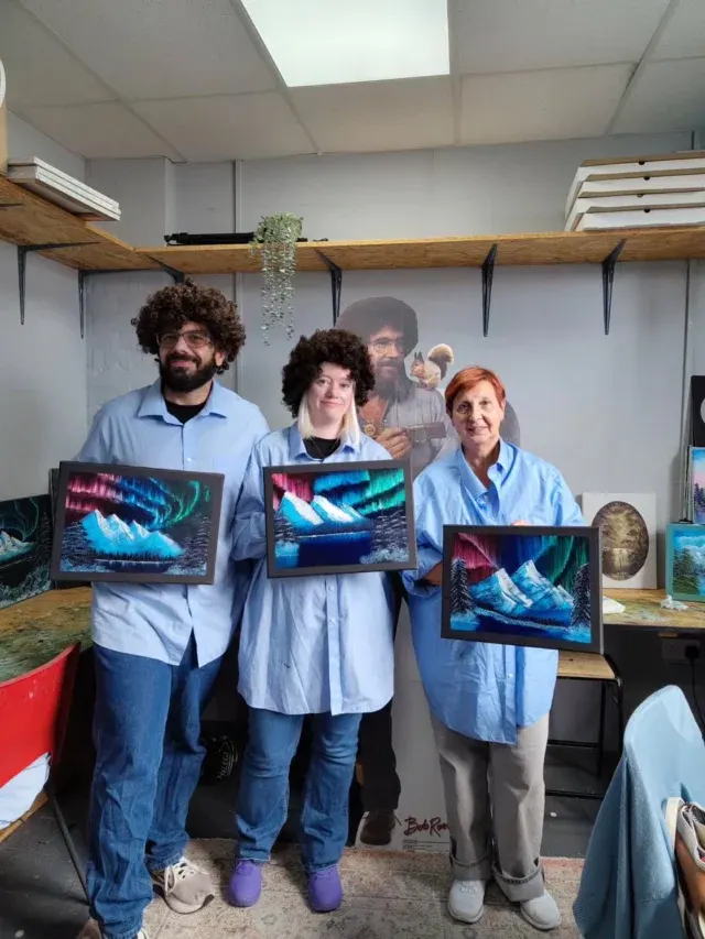 Three people in a studio holding framed digital artwork displays with colourful wave patterns.