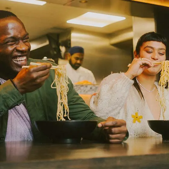 Two people enjoying noodles together at a counter in a casual dining restaurant.