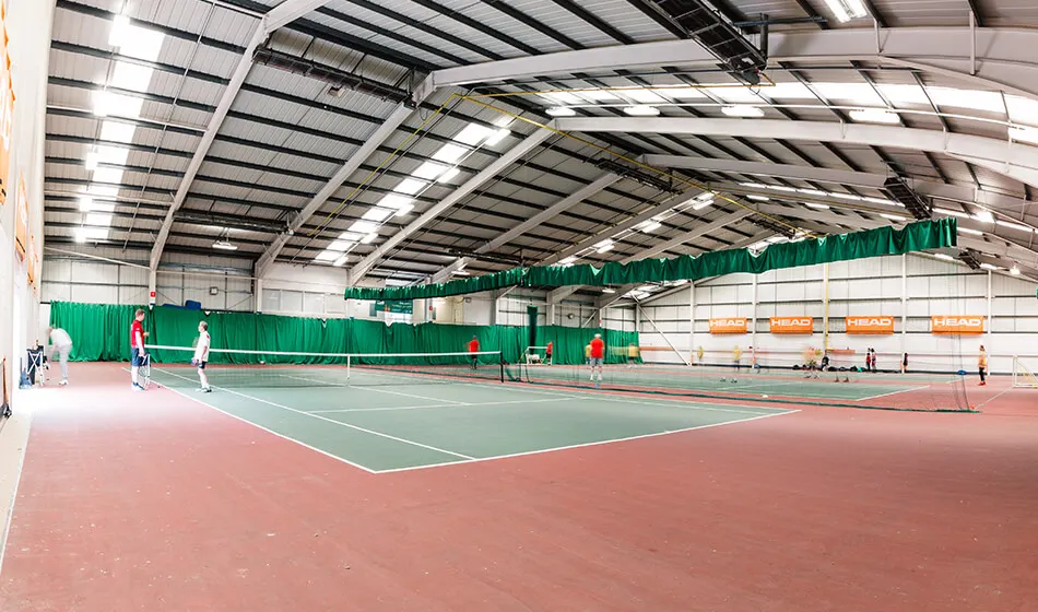 Indoor tennis court with players and coaches during a training session.