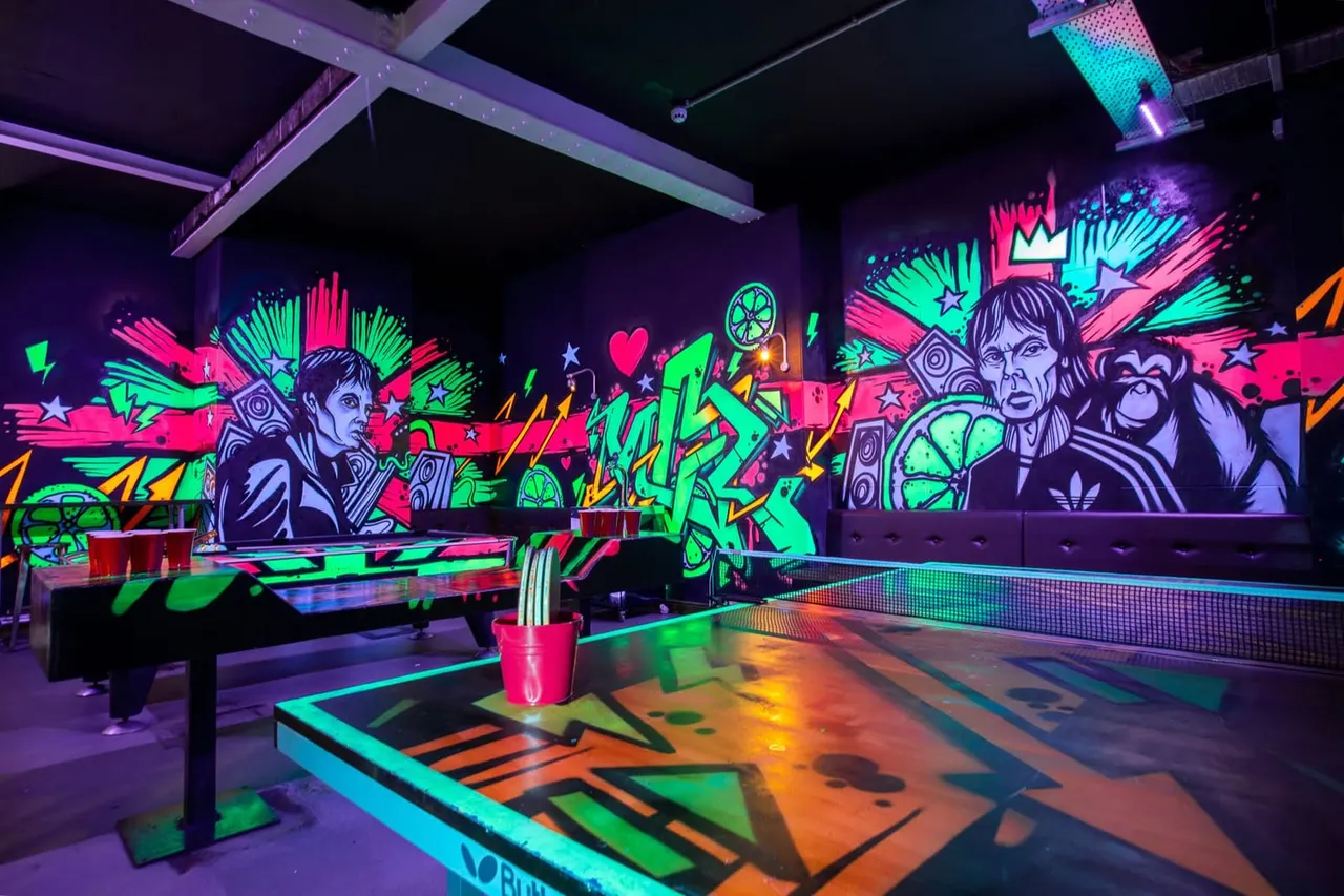 Vibrant neon-lit indoor mini golf course with colourful graffiti-style wall art and fluorescent floor designs.